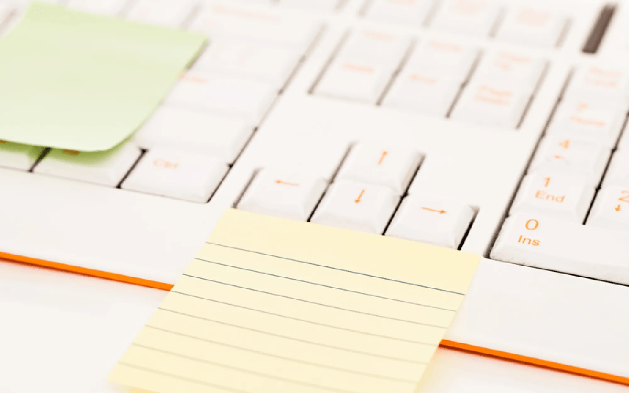 Gelbe und grüne Post-it-Zettel kleben auf einer weißen Computertastatur, die leicht seitlich aufgenommen wurde.