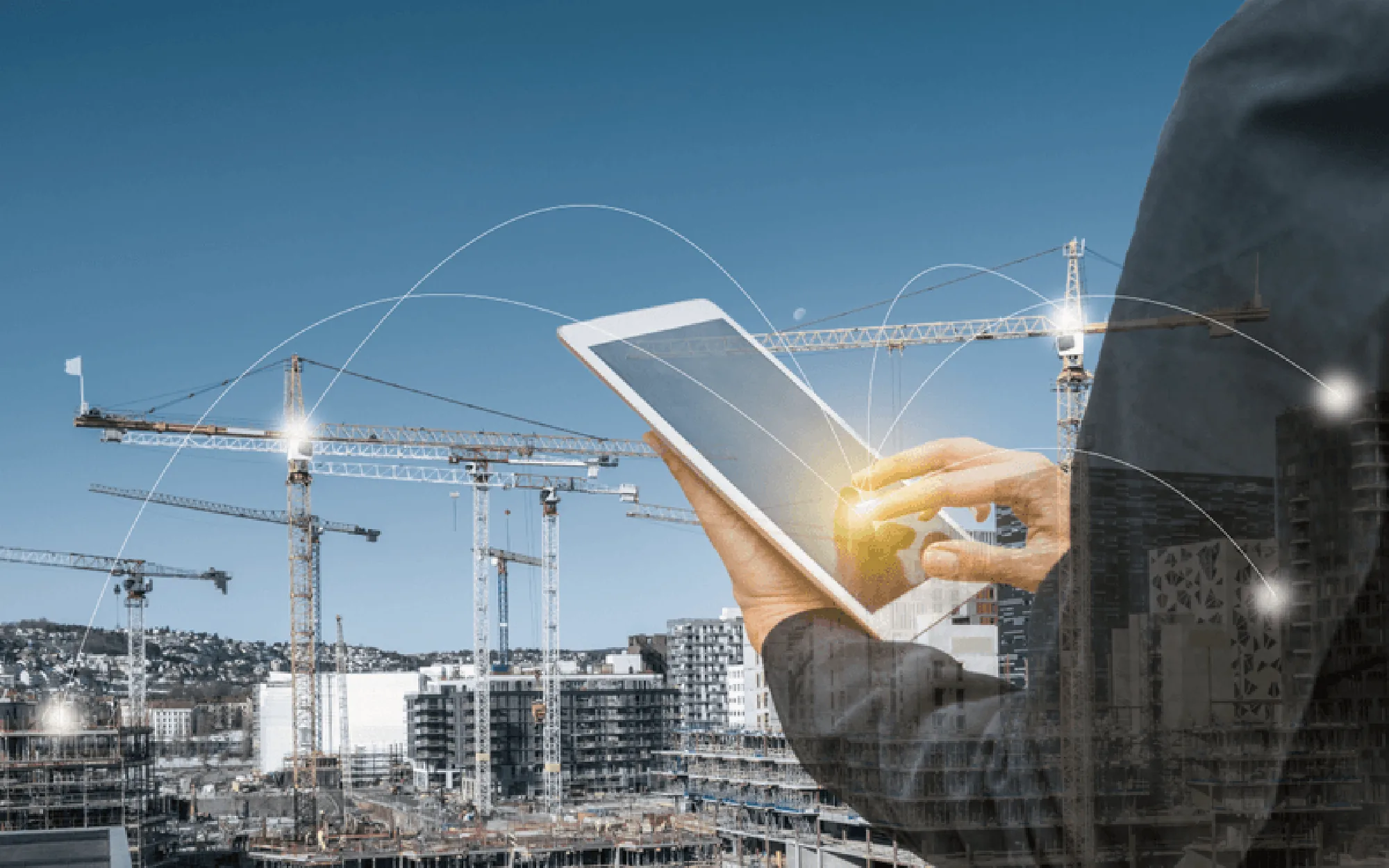 Eine Person verwendet ein Tablet zur digitalen Planung auf einer Baustelle mit mehreren Kränen im Hintergrund.