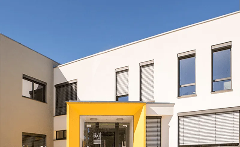 Gebäude der Max Netter GmbH (Netter Bau Art) mit weißer Fassade und gelb eingefasstem Eingang.